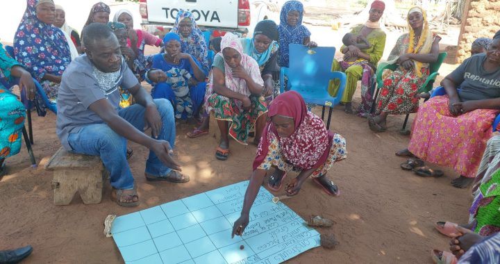 A woman marks a community mapping chart on the ground during a participatory research session