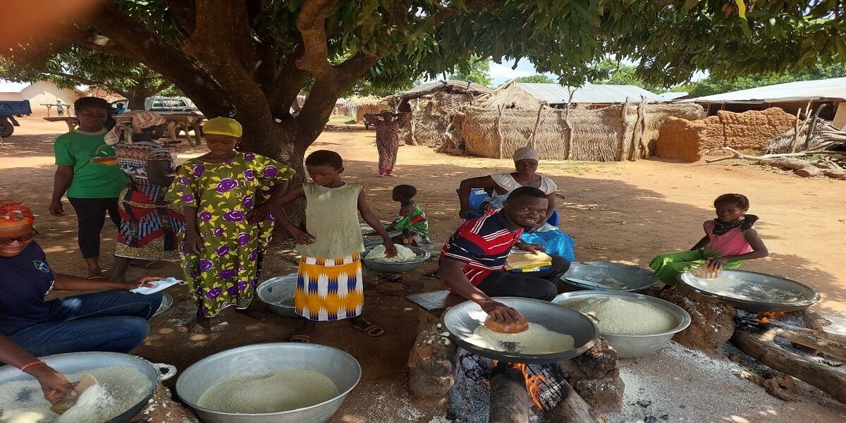 Community members roasting cassava into gari over open fires in a village