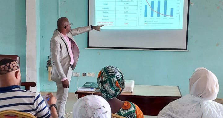 A facilitator presenting research findings on a projector screen to seated community members